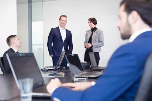 Successful team leader and business owner leading informal in-house business meeting. Businessman working on laptop in foreground. Business and entrepreneurship concept.