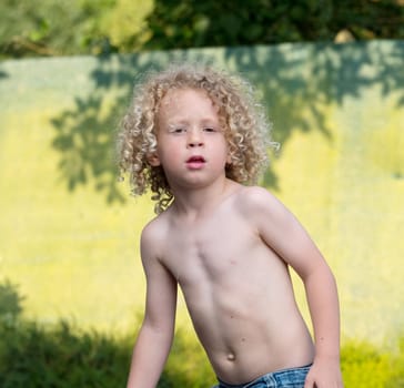 little blond boy shirtless playing in the garden