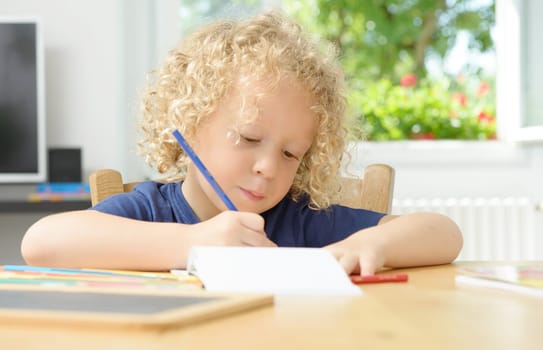 a little blond boy drawing in his home