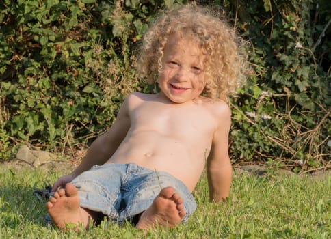 little blond boy shirtless playing in the garden