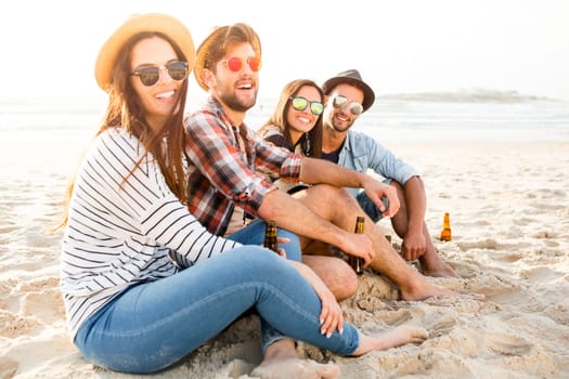Friends having fun together at the beach and drinking a cold beer