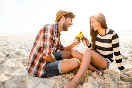 Young couple at the beach having fun, laughing and drinking beer