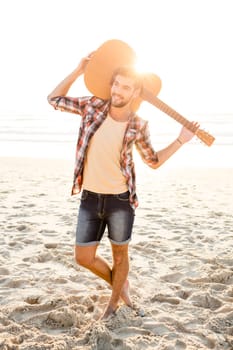 Portrait of a handsome young man with his guitar at the beach