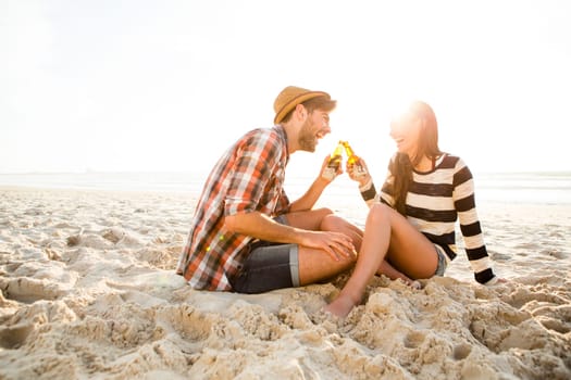 Young couple at the beach having fun, laughing and drinking beer