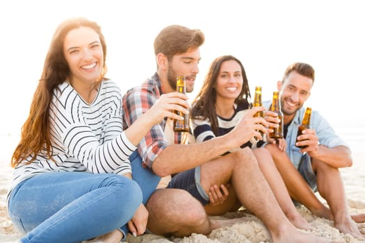 Friends having fun together at the beach and drinking a cold beer