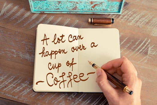 Handwritten text A Lot Can Happen Over A Cup Of Coffee as business image. Retro effect and toned image of a woman hand writing a note with fountain pen on a notebook.
