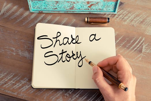 Handwritten text Share A Story as business image. Retro effect and toned image of a woman hand writing a note with fountain pen on a notebook.