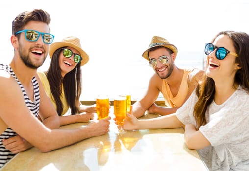Friends having fun and drinking a cold beer at the beach bar