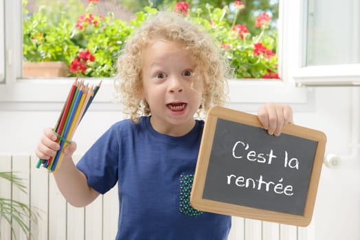 blond and curly boy holding a blackboard written back to school