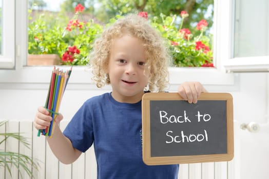 blond and curly boy holding a blackboard written back to school