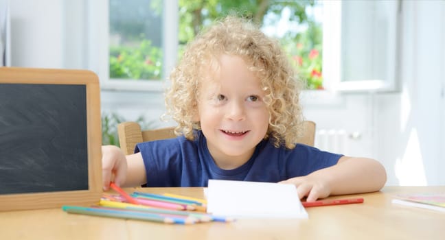 a blond boy drawing on a notebook in his home