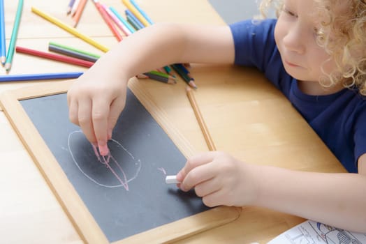 a blond boy drawing on a blackboard