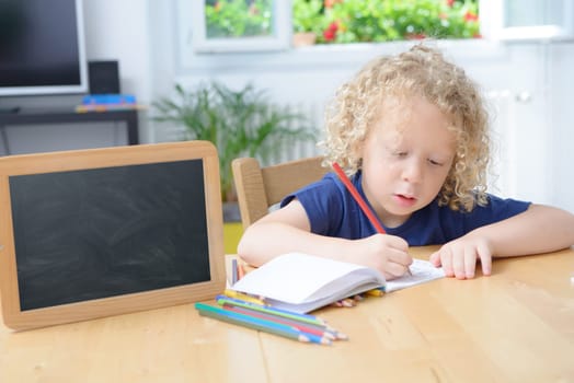 a blond boy drawing on a notebook in his home