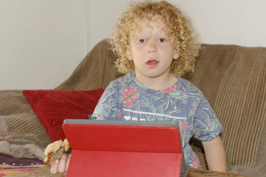 a blond boy playing with a digital tablet, in home
