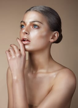 Portrait of a woman with golden skin. She looks up, a finger touches the lips.