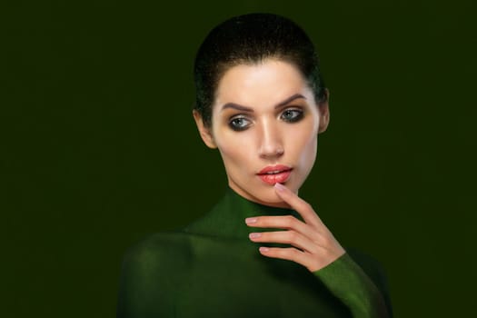 Portrait of a beautiful woman on a green background. Close-up face. think. Thumb near the lips.