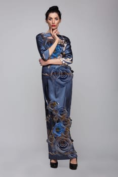 Beautiful female model posing in elegant long dress with flowers in studio.