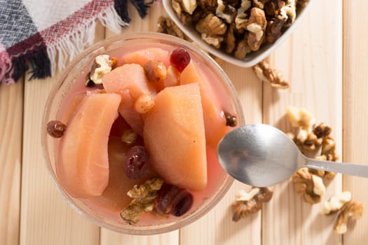 Apple compote with dried fruits in the cup on wooden table with decorative wallnuts