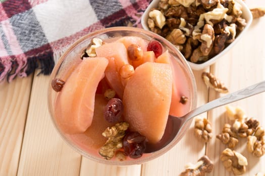 Apple compote with dried fruits in the cup on wooden table with decorative wallnuts