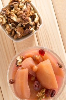 Apple compote with dried fruits in the cup on wooden table with decorative wallnuts