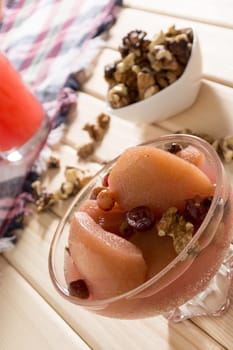 Apple compote with dried fruits in the cup on wooden table with decorative wallnuts