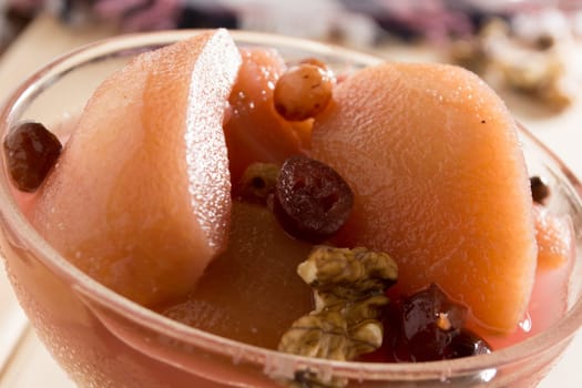 Apple compote with dried fruits in the cup on wooden table with decorative wallnuts