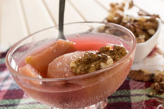Apple compote with dried fruits in the cup on wooden table with decorative wallnuts