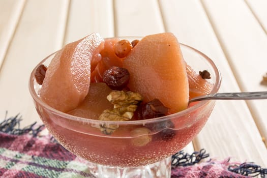 Apple compote with dried fruits in the cup on wooden table with decorative wallnuts