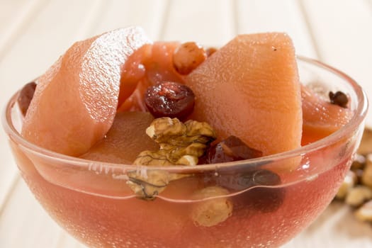 Apple compote with dried fruits in the cup on wooden table with decorative wallnuts