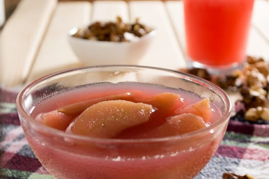 Apple compote with dried fruits in the cup on wooden table with decorative wallnuts