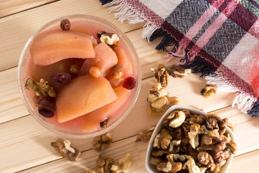 Apple compote with dried fruits in the cup on wooden table with decorative wallnuts