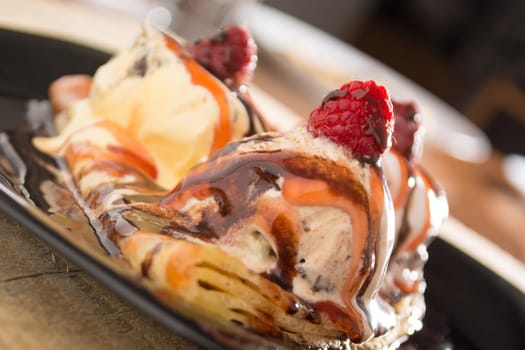 Fresh, golden pancakes with fruit and cream on a black plate with blurred background