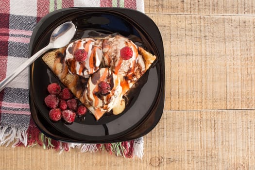 Fresh, golden pancakes with fruit and cream on a black plate with blurred background