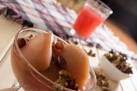 Apple compote with dried fruits in the cup on wooden table with decorative wallnuts