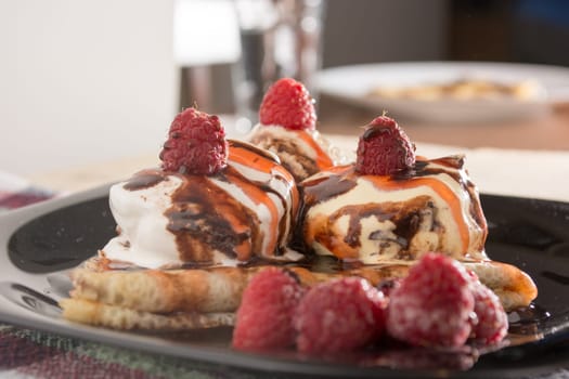 Fresh, golden pancakes with fruit and cream on a black plate with blurred background