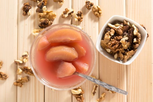 Apple compote with dried fruits in the cup on wooden table with decorative wallnuts