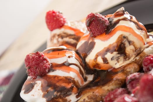 Fresh, golden pancakes with fruit and cream on a black plate with blurred background