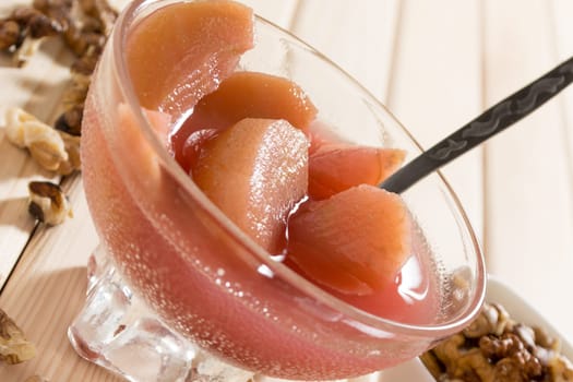 Apple compote with dried fruits in the cup on wooden table with decorative wallnuts