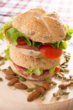 Stacked sandwiches with fresh smoked meat, cheese, lettuce and tomato with homemade ketchup arranged with almond and pumpkin seeds