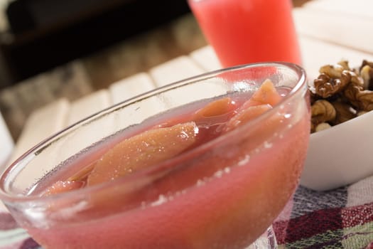Apple compote with dried fruits in the cup on wooden table with decorative wallnuts