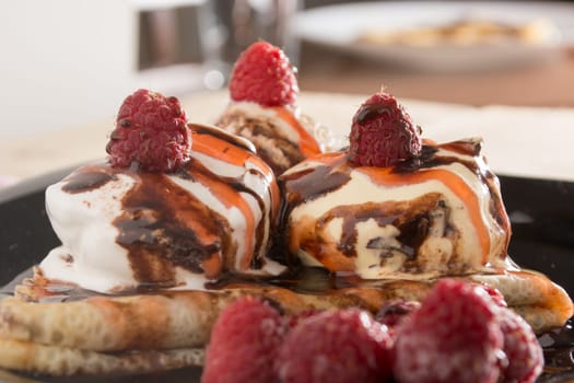 Fresh, golden pancakes with fruit and cream on a black plate with blurred background