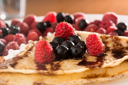 Fresh pancakes with fruit arranged all over it, and with cream