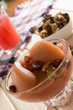 Apple compote with dried fruits in the cup on wooden table with decorative wallnuts