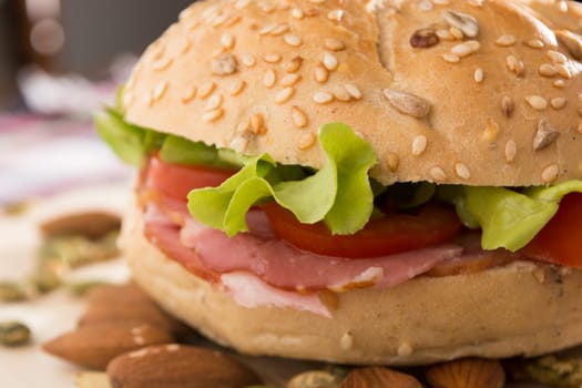 Sandwich with fresh smoked meat, cheese, lettuce and tomato with homemade ketchup arranged with almond and pumpkin seeds