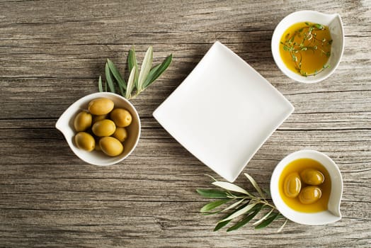 Olive oil with fresh herbs and plate on wooden background.
