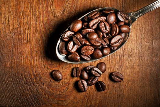 Coffee beans in spoon on wooden background.