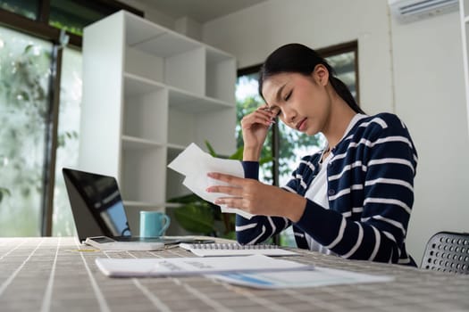 A young woman appears stressed while managing her bills and finances at home, reflecting the challenges of budgeting and financial management.