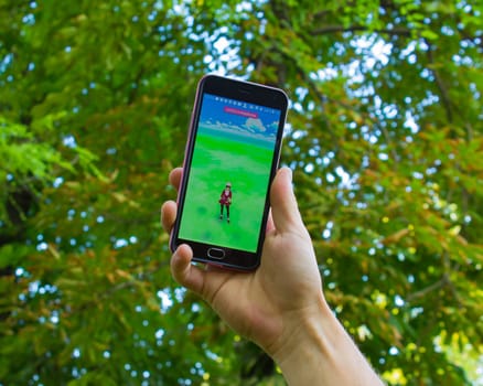 Dnipropetrovsk, Ukraine - July 23, 2016: The male hand holding phone with game Pokemon GO - a free-to-play augmented reality mobile game developed by Niantic for iOS and Android devices.