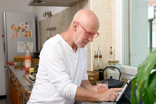 a senior man in kitchen using digital tablet and drink fruit juice