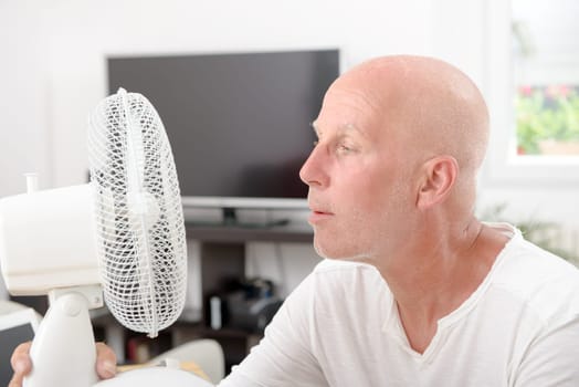 mature man refreshed with a fan in his home